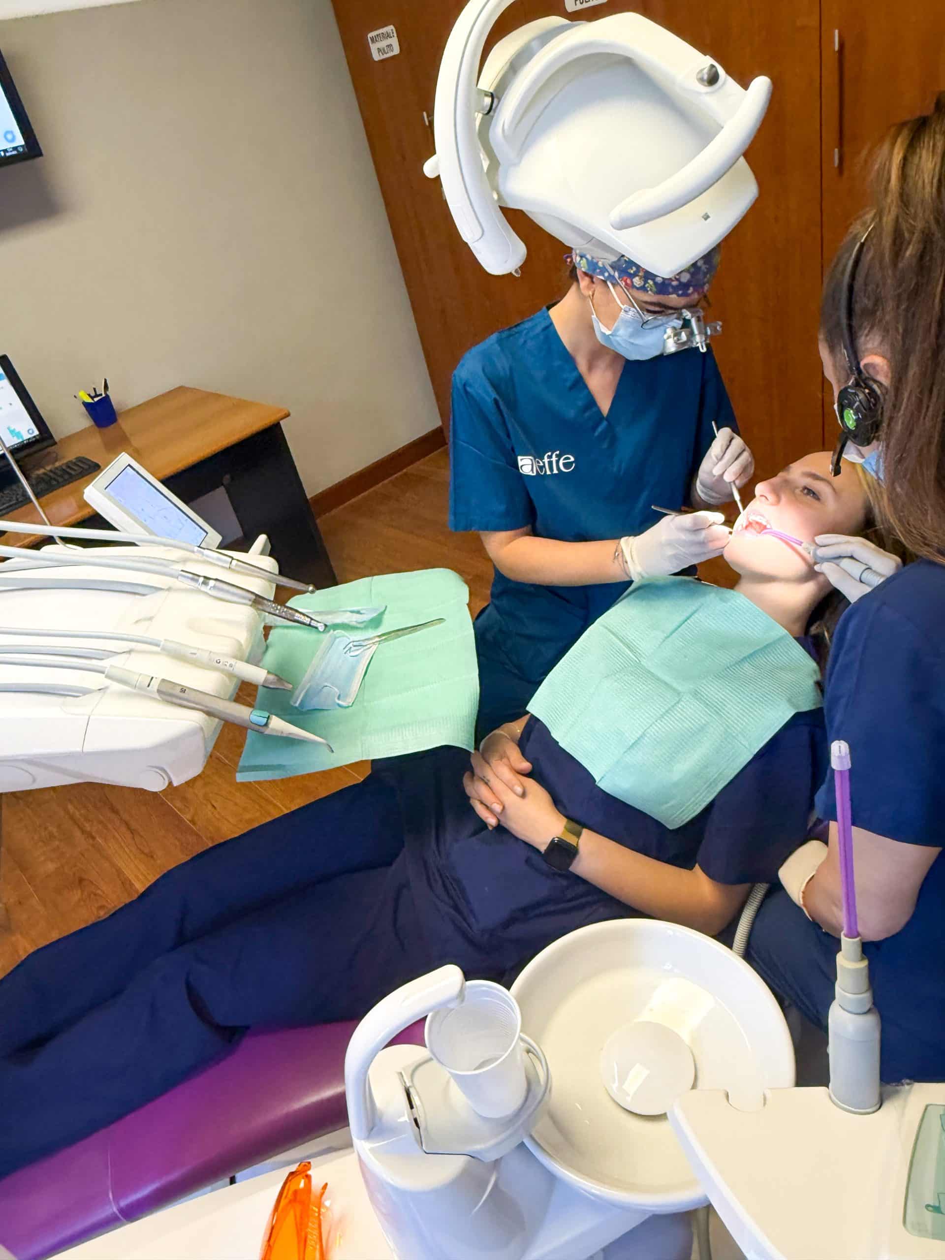 Dentista e assistente curano paziente su poltrona odontoiatrica.