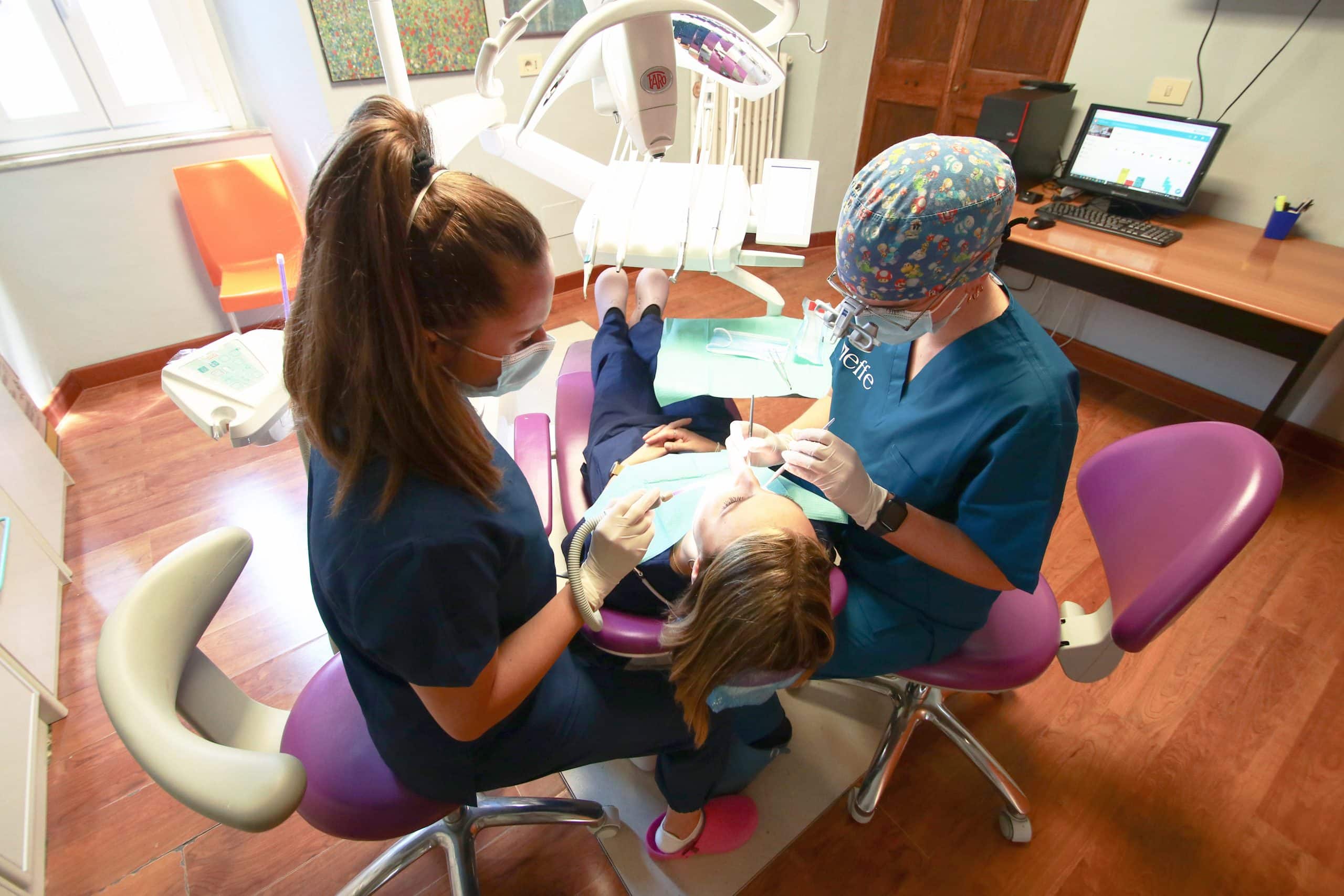 Dentista e assistente curano paziente su poltrona odontoiatrica.