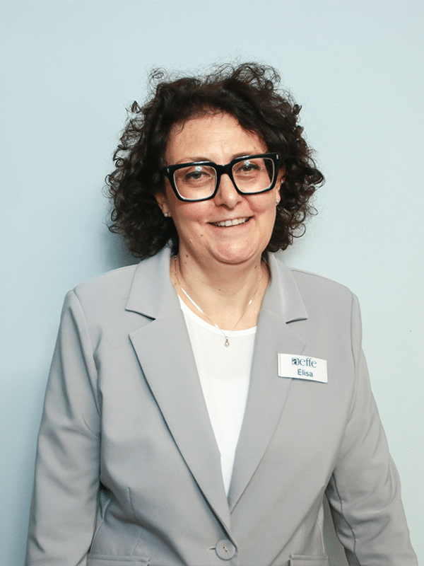 Donna con occhiali e giacca grigia, sfondo azzurro.